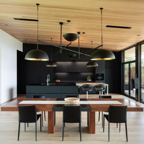 alt="full kitchen and dining room view of floor-to-ceiling slate black fenix cabinets with color matched matte glass countertop and contrasting warm wood tones"