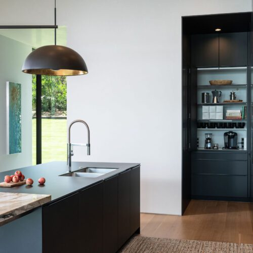 alt=”opposite island view showing slate black Fenix cabinets, sink, and hidden appliance cabinet with floor-to-ceiling slate black cabinets”