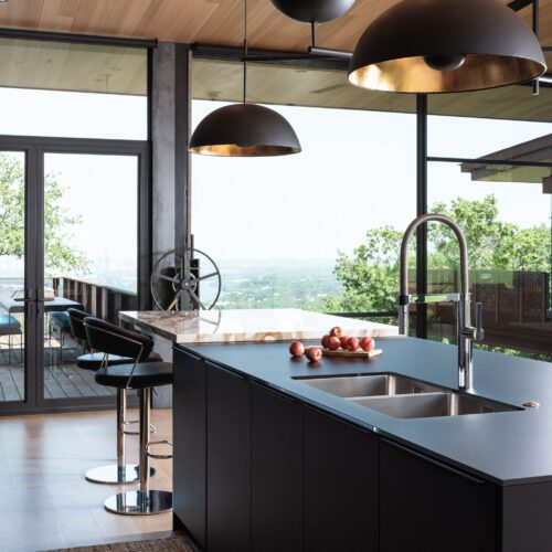 alt=”corner view of kitchen island with slate black Fenix cabinets, color matched matte glass countertop, and integrated contrasting tabletop”